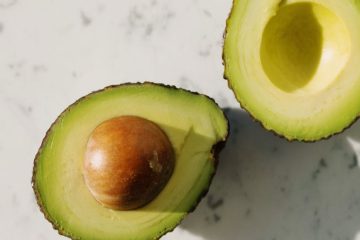 halves of fresh green avocado on marble surface