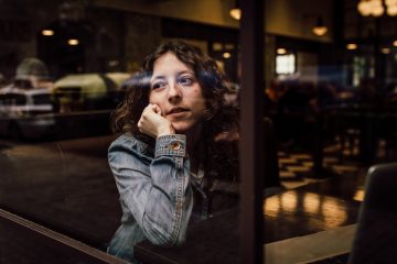 woman wearing blue denim jacket putting her right arm on her cheek