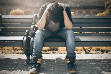 man in black shirt and gray denim pants sitting on gray padded bench