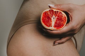 woman holding a red orange next to her hip