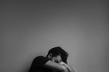 grayscale photography of man sitting beside wall