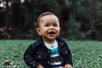 photo of smiling baby boy in denim outfit sitting on grass