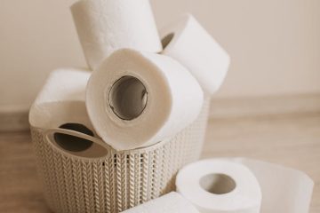 tubes of white toilet paper and plastic basket on bathroom floor