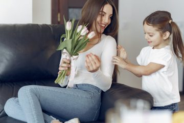 happy mother and daughter giving flowers to mother at home