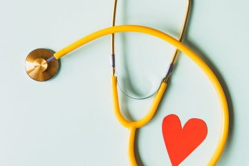 medical stethoscope with red paper heart on white surface