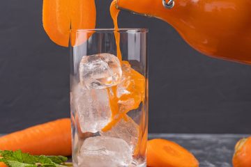 a person pouring carrot juice in the glass