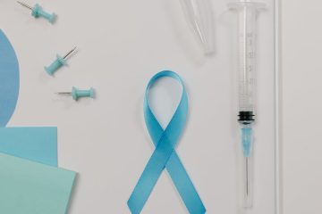 a blue ribbon symbol for prostate cancer beside a syringe on white surface